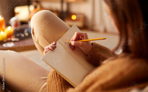 halloween, holidays and leisure concept - close up of young woman with pencil writing to diary and resting her feet on table at cozy home photo