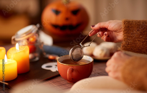 drinks, holidays and leisure concept - woman's hand with mesh tea infuser ball and mug at home on halloween photo