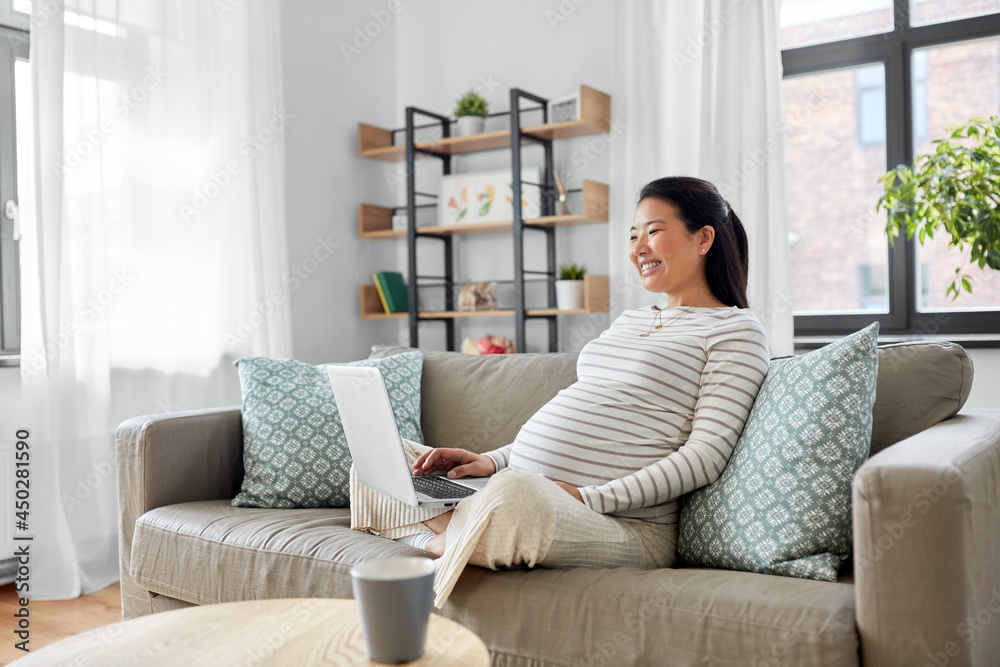 pregnancy, rest, people and expectation concept - happy smiling pregnant asian woman with laptop computer sitting on sofa at home pregnancy, rest, people and expectation concept - happy smiling pregnant asian woman with laptop computer sitting on sofa at home
