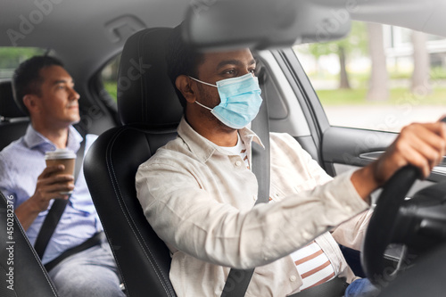 transportation, health and people concept - male passenger with cup of takeaway coffee and indian taxi driver wearing face protective mask for protection from virus disease driving car