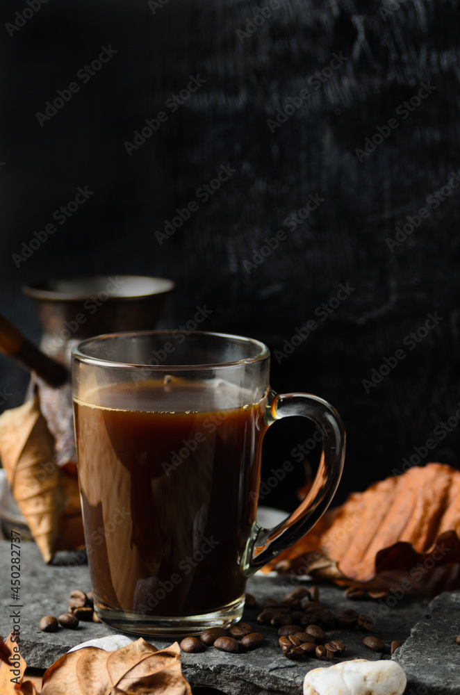 A glass mug of strongly brewed coffee on the stones with coffee beans and autumn leaves A glass mug of strongly brewed coffee on the stones with coffee beans and autumn leaves