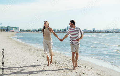 summer holidays and people concept - happy couple running along beach