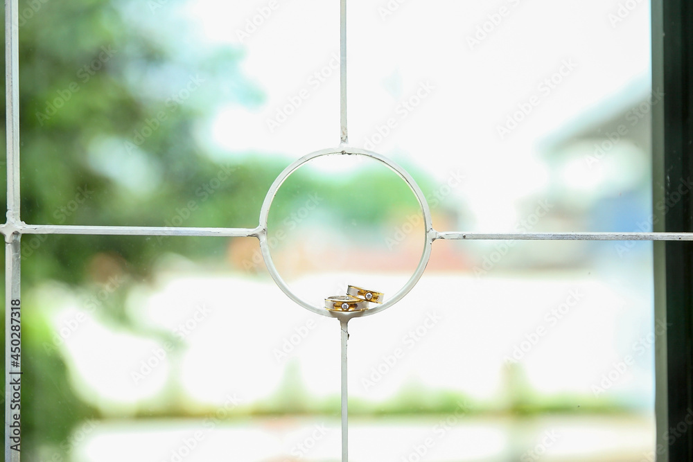 Close up of stacked wedding rings of groom and bride on window grating with bokeh background. Selective focus. Wedding photography concept. No people.