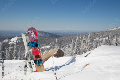 Snowboard and downhill skis are standing in a snowdrift on the top of the mountain.