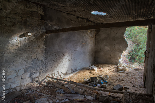 Abandoned old barn in a village interior with debris and sunlight falling through broken wall and roof
