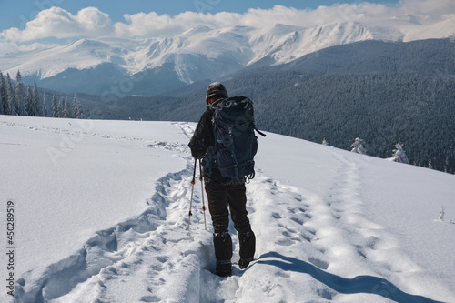 Man backpacker hiking snowy mountain hillside on cold winter day.