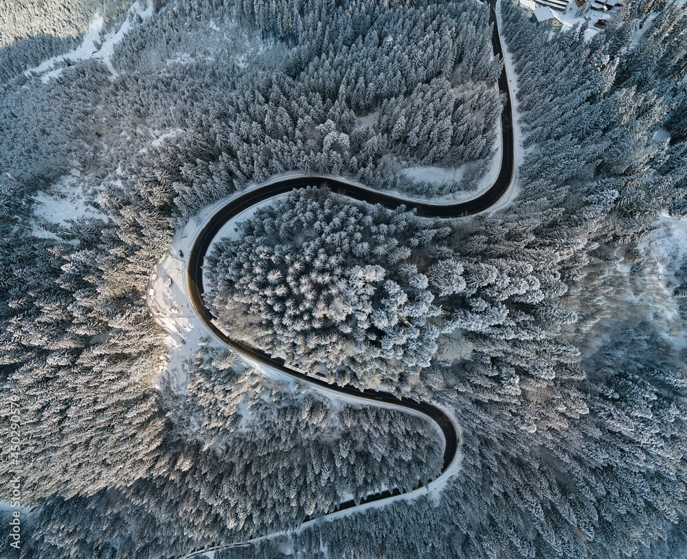 Aerial view of winter landscape with snow covered mountain hills and winding forest road in morning.