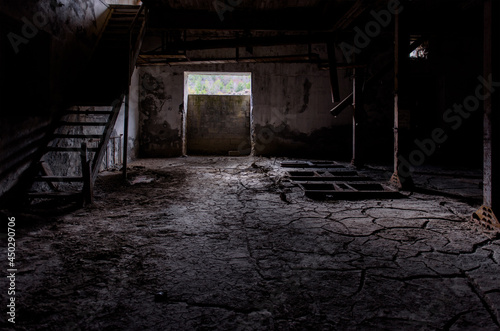 Old factory interior backdrop. Dark room with cracked dirt on the floor, broken wooden stairs and rusty remains of machinery photo