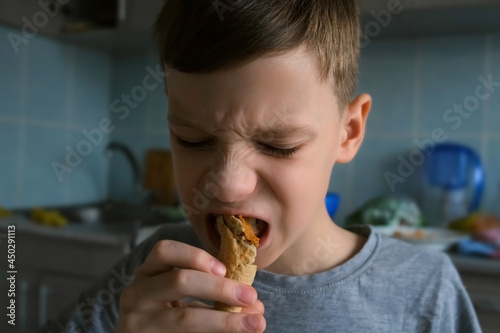 Portrait of child teen boy is enjoying of eating ice cream in a cone in kitchen at home. Harmful sweet food that children love. He is dirty and it s got chocolate on his face.