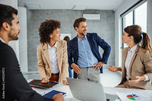 Multicultural group of business people standing in boardroom and having meeting about project. Group looking at businesswoman explaining her idea.