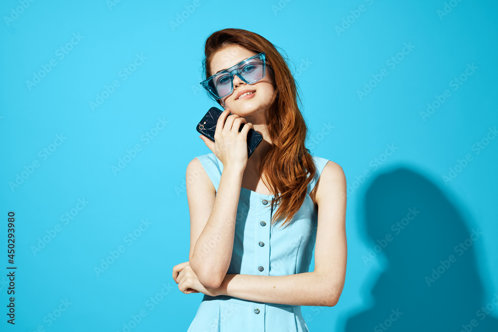 portrait of a woman in a dress and glasses with phone in hand blue background portrait of a woman in a dress and glasses with phone in hand blue background