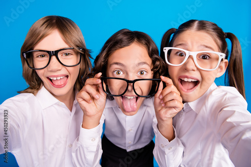 Photo of funny foolish crazy schoolkids look camera show tongue wear glasses uniform isolated blue color background