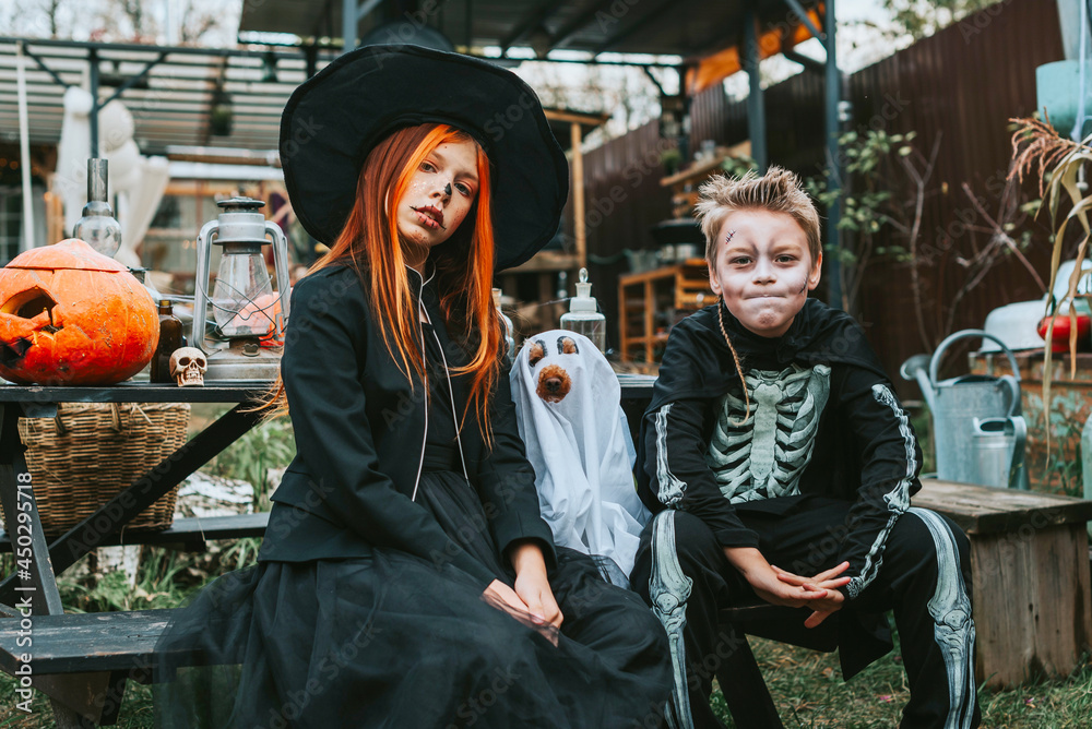 children a boy in a skeleton costume and a teenage girl in a witch costume having fun at a Halloween party on the decorated porch suburban house
