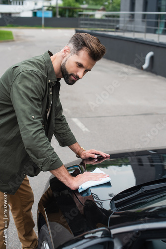 Young man in casual clothes wiping car outdoors