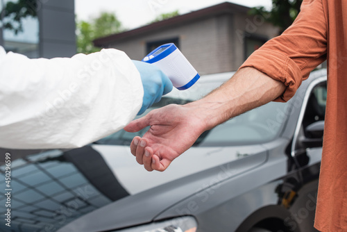 Cropped view of medical worker holding pyrometer near driver and car