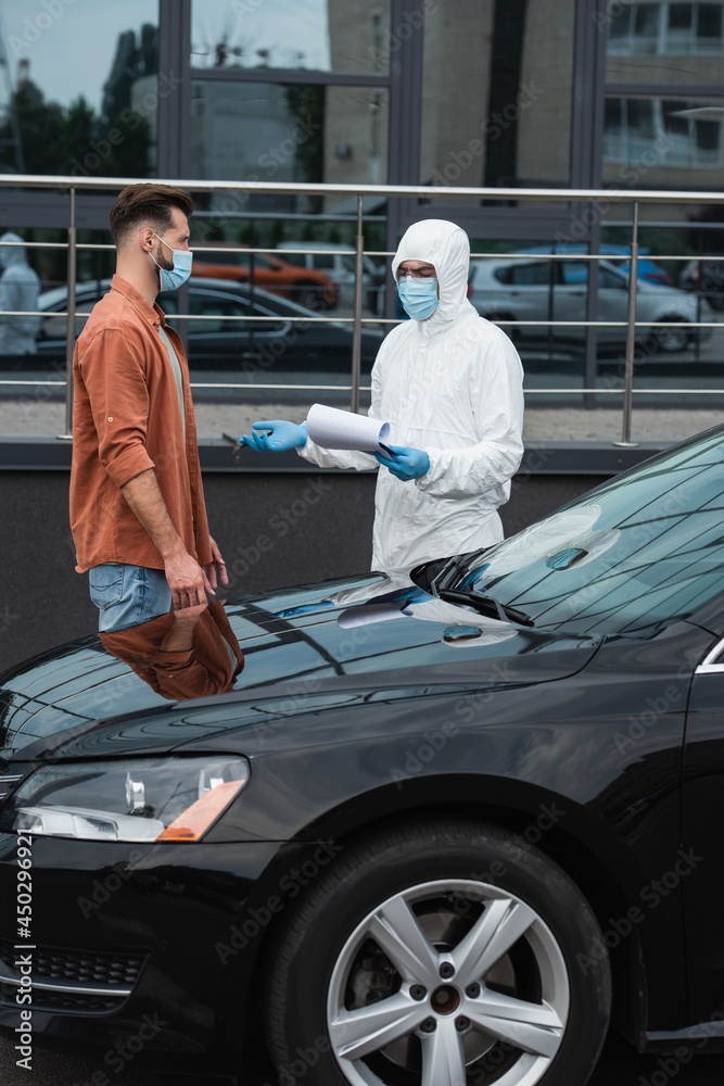 Naklejka premium Driver in mask standing near medical worker with clipboard pointing with hand outdoors
