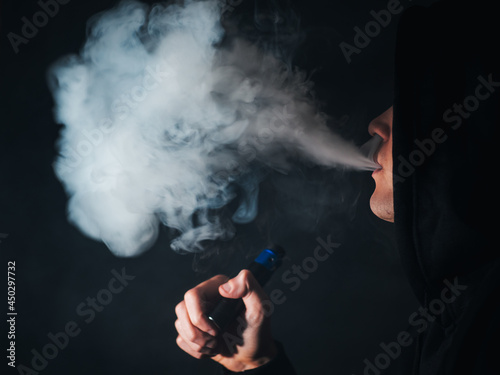 A young man exhales a cloud of steam using an electronic cigarette. Alternative methods of obtaining nicotine