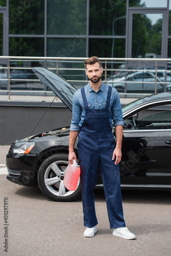 Repairman in overalls holding windshield washer fluid near auto outdoors © LIGHTFIELD STUDIOS