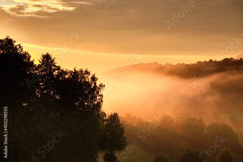 Beautiful rural summer landscape with trees, fog and a hill during sunset. Seen in Germany in the Rhön Mountains near Gersfeld in summer
