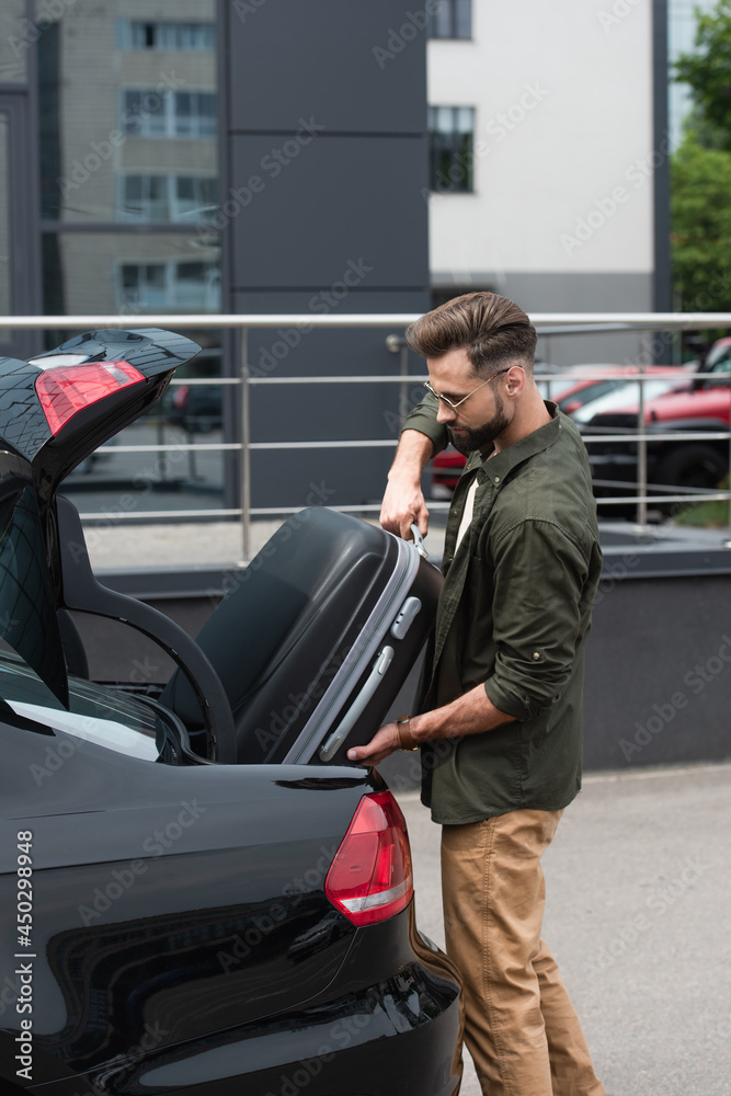 Side view of man in sunglasses putting suitcase in trunk of car Side view of man in sunglasses putting suitcase in trunk of car