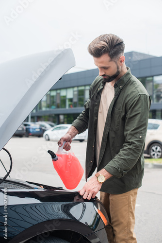 Driver pouring antifreeze near car with open trunk photo