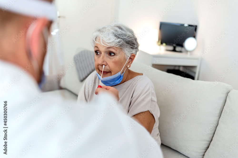 Obraz premium Modern laboratory worker wearing personal protective equipment testing senior woman for coronavirus using nasal swab method. Close up of a elderly woman having a nasal swab test done by her doctor.