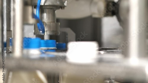 Close up Installation and capping of blue plastic lids on plastic bottles filled with dairy products on a conveyor machine.