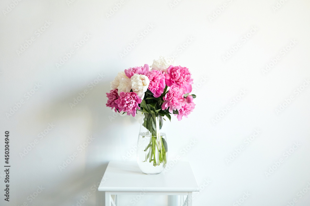 Empty white wall with pink flowers. Peonies in a glass vase in a bright interior