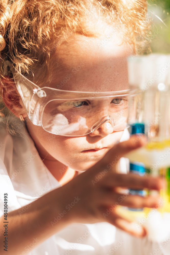 Close up of a little red-haired girl in white uniform conducting chemical experiments in laboratory.Back to school concept.Young scientists.Natural sciences.Preschool and school education of children. Close up of a little red-haired girl in white uniform conducting chemical experiments in laboratory.Back to school concept.Young scientists.Natural sciences.Preschool and school education of children.