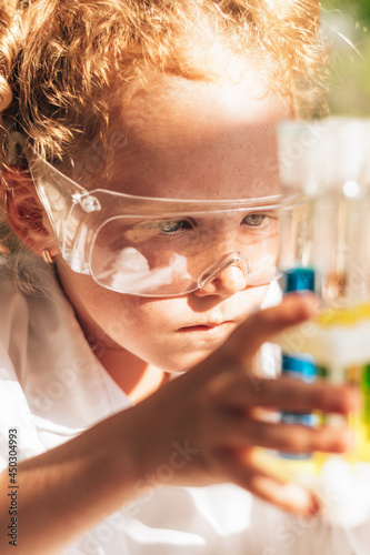 Close up of a little red-haired girl in white uniform conducting chemical experiments in laboratory.Back to school concept.Young scientists.Natural sciences.Preschool and school education of children.