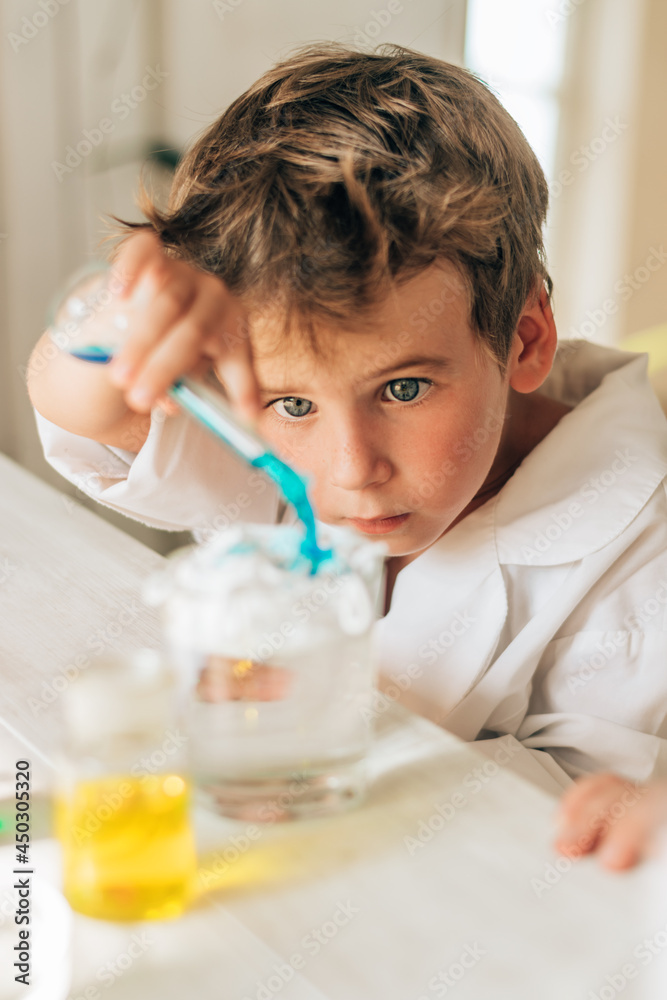 Curious little boy in white uniform conducts chemical experiments in a laboratory.Back to school concept.Young scientists.Natural sciences.Preschool and school education of children. Curious little boy in white uniform conducts chemical experiments in a laboratory.Back to school concept.Young scientists.Natural sciences.Preschool and school education of children.
