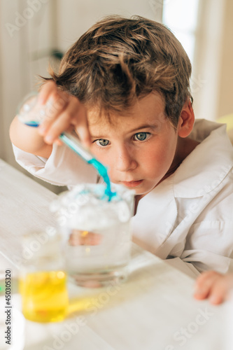 Curious little boy in white uniform conducts chemical experiments in a laboratory.Back to school concept.Young scientists.Natural sciences.Preschool and school education of children.