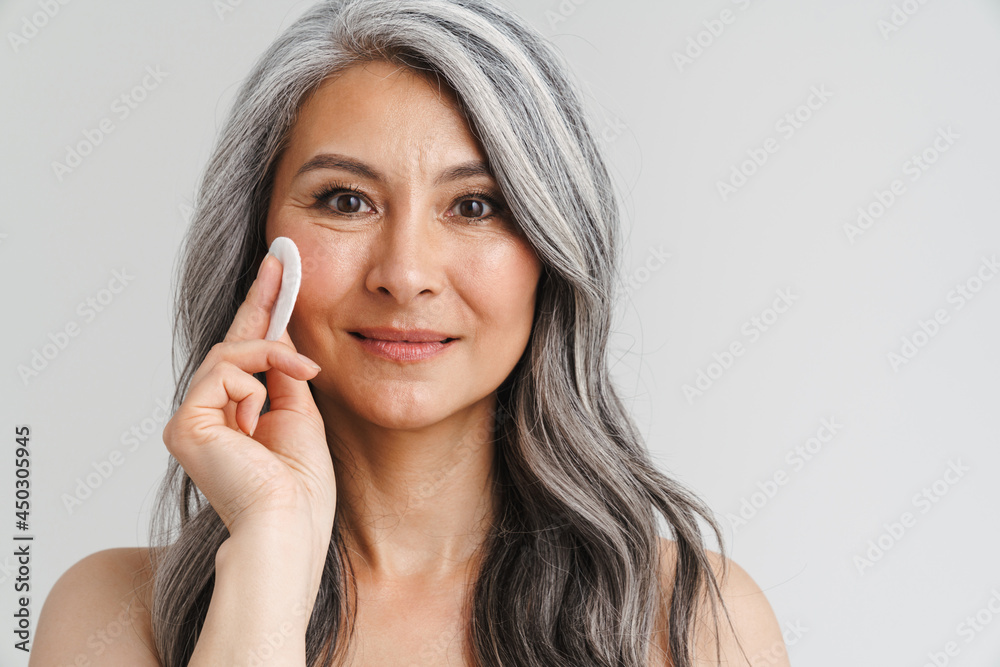 Mature shirtless woman with grey hair using cotton pad Mature shirtless woman with grey hair using cotton pad