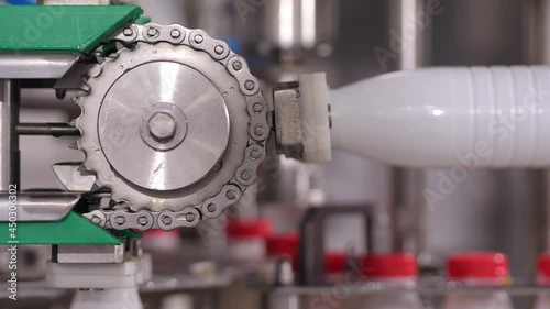 Production of milk or yogurt factory. The wet bottles move along the conveyor belt. Ordering and completing of finished products. Lining up filled plastic bottles with a red lid. Close up.