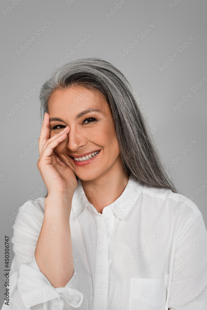 cheerful middle aged woman holding hand near face while smiling at camera isolated on grey cheerful middle aged woman holding hand near face while smiling at camera isolated on grey