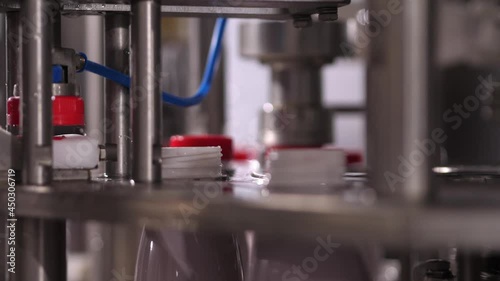 Close up Installation and capping of red plastic lids on plastic bottles filled with dairy products on a conveyor machine.