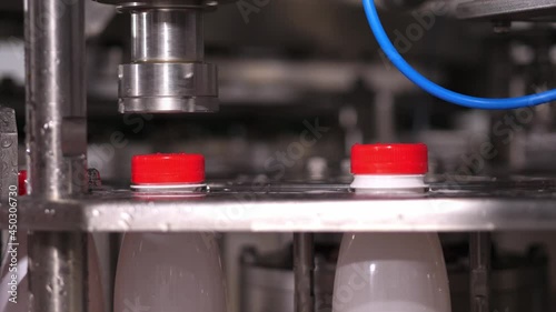 Close up Installation and capping of red plastic lids on plastic bottles filled with dairy products on a conveyor machine.