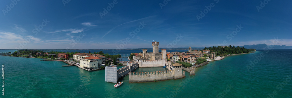 Italian castles Scaligero on the water. Aerial panorama of Sirmione castle, Lake Garda, Italy. Flag of Italy on the towers of the castle on Lake Garda. Top view of the 13th century castle.