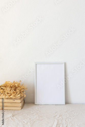Home decor mock-up, blank picture frame near white painted concrete wall , dried yellow oat stalks and old books