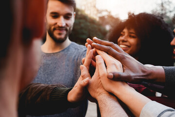 Multiracial young people celebrating together while stacking hands outdoor - Focus on hands