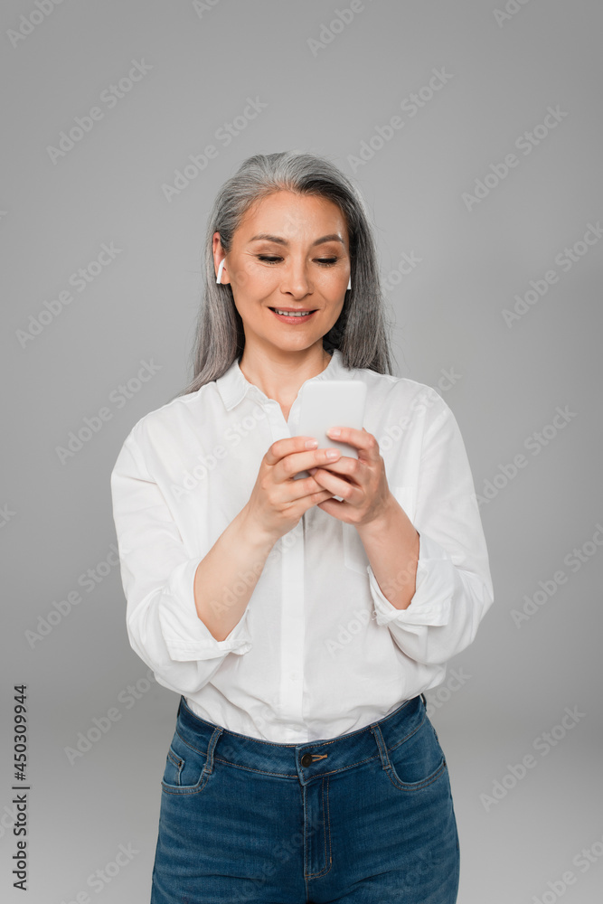 positive middle aged woman in earphones using smartphone isolated on grey positive middle aged woman in earphones using smartphone isolated on grey