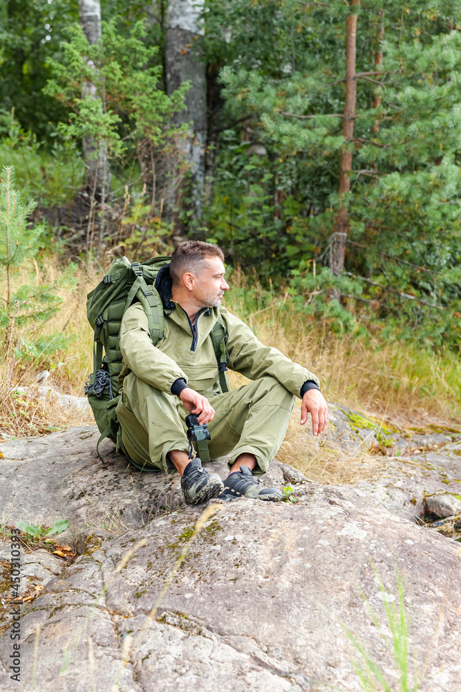 Young man travelling alone with a backpack. Concept of active tourism, camping in the forecast, trekking and hiking during vacations. Green background. Copy space for text