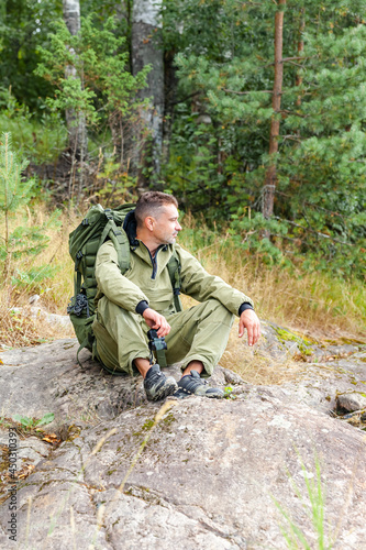 Young man travelling alone with a backpack. Concept of active tourism, camping in the forecast, trekking and hiking during vacations. Green background. Copy space for text