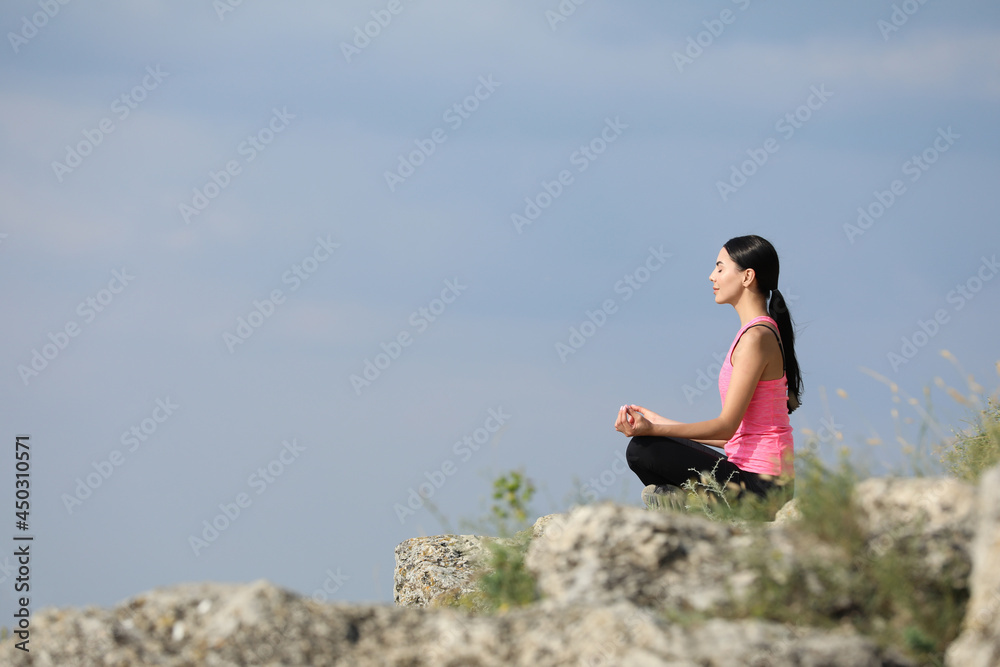 Young woman meditating on cliff. Space for text