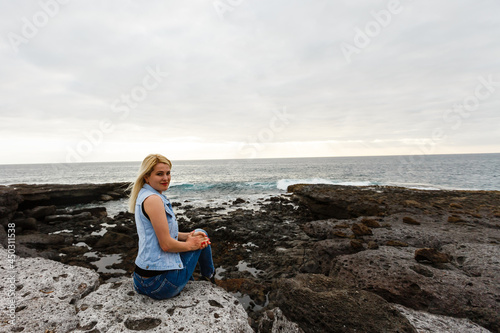 Women on volcanic rocks and blue ocean with waves, white foam and volcanic rocks. Canary Islands. The magnificent coast of the Atlantic Ocean