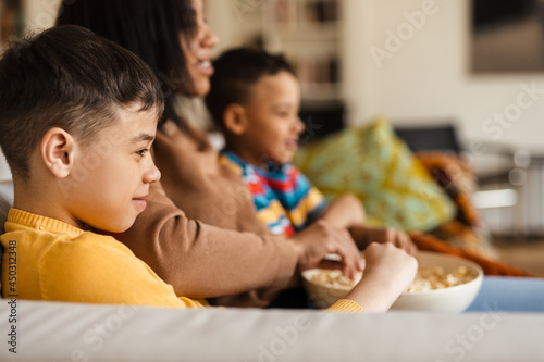 Two boys and their mother watching movie while eating popcorn in home