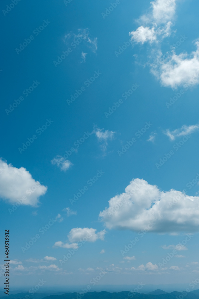 Obraz premium Blue Ridge Mountains of North Carolina, USA looking tiny and distant under striking blue sky with puffy white clouds