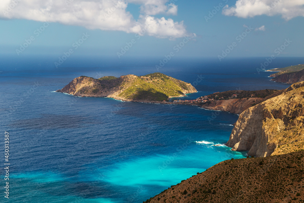 Fototapeta premium Aerial view at Asos village, Assos peninsula and fantastic turquoise and blue Ionian Sea water. Top view, summer scenery of famous and extremely popular travel destination in Cephalonia, Greece