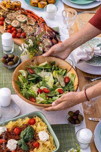 Hands of young woman putting bowl with vegetarian salad on table served for family dinner