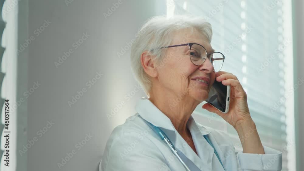Mature doctor with glasses talks on phone in hospital office Mature doctor with glasses talks on phone in hospital office